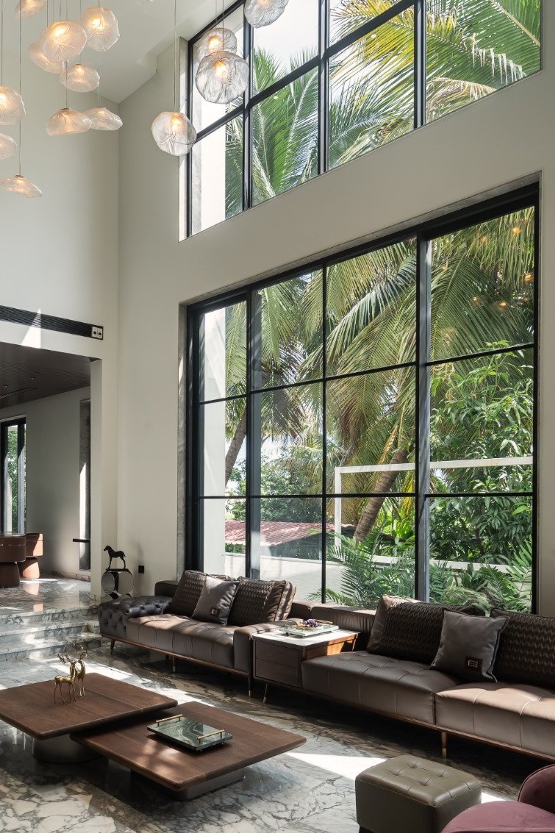 Harshana Residence: the living room, with the retained coconut trees outside the double-height windows.